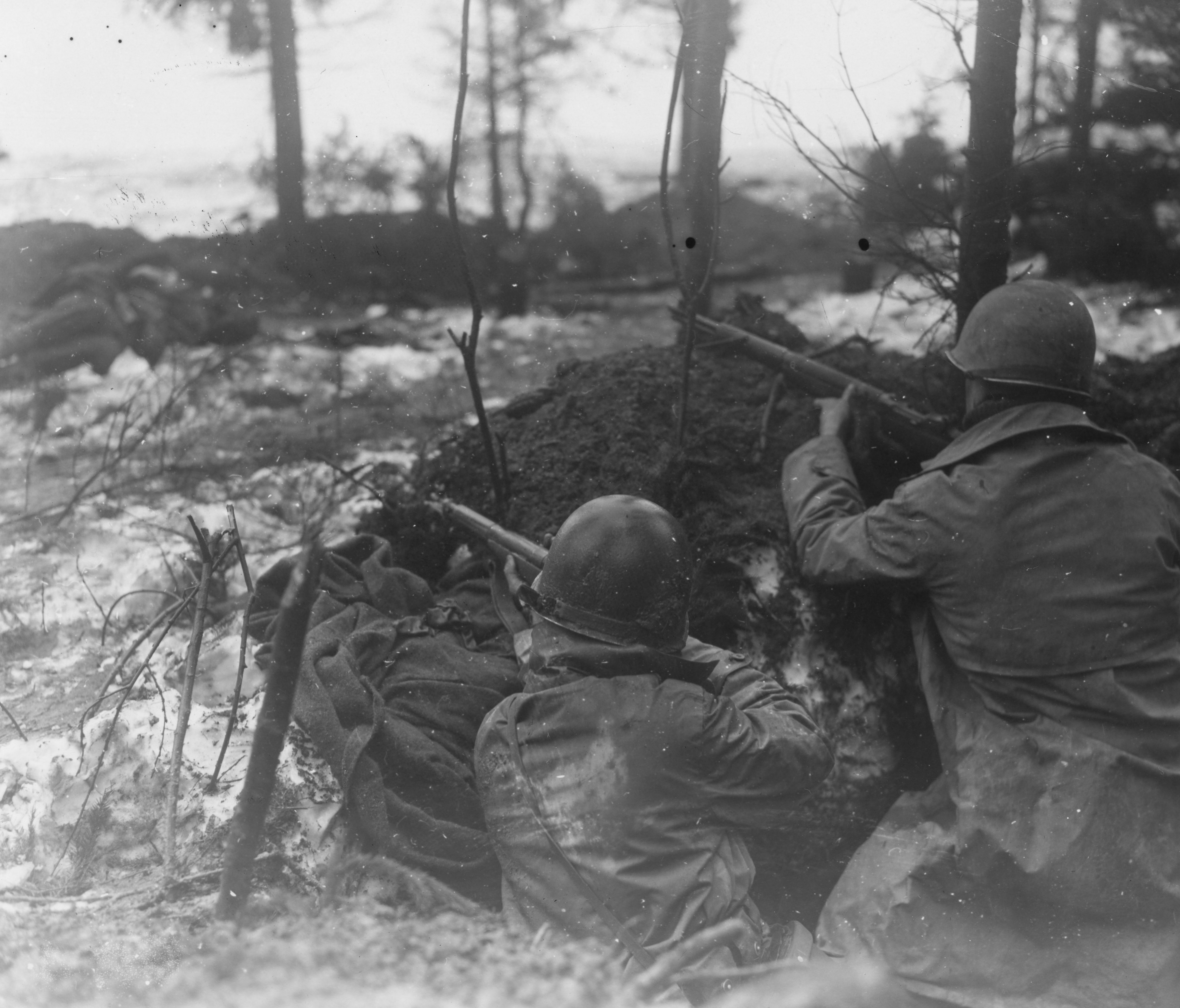 Two riflemen of the 99th Infantry Division on watch in a snow-rimmed, log-reinforced foxhole near Rocherath, Belgium, winter 1945.