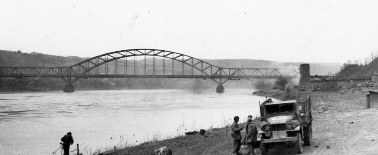 Side view of the Ludendorff Bridge at Remagen with smoke rising from German artillery fire below and behind it, March 1945.