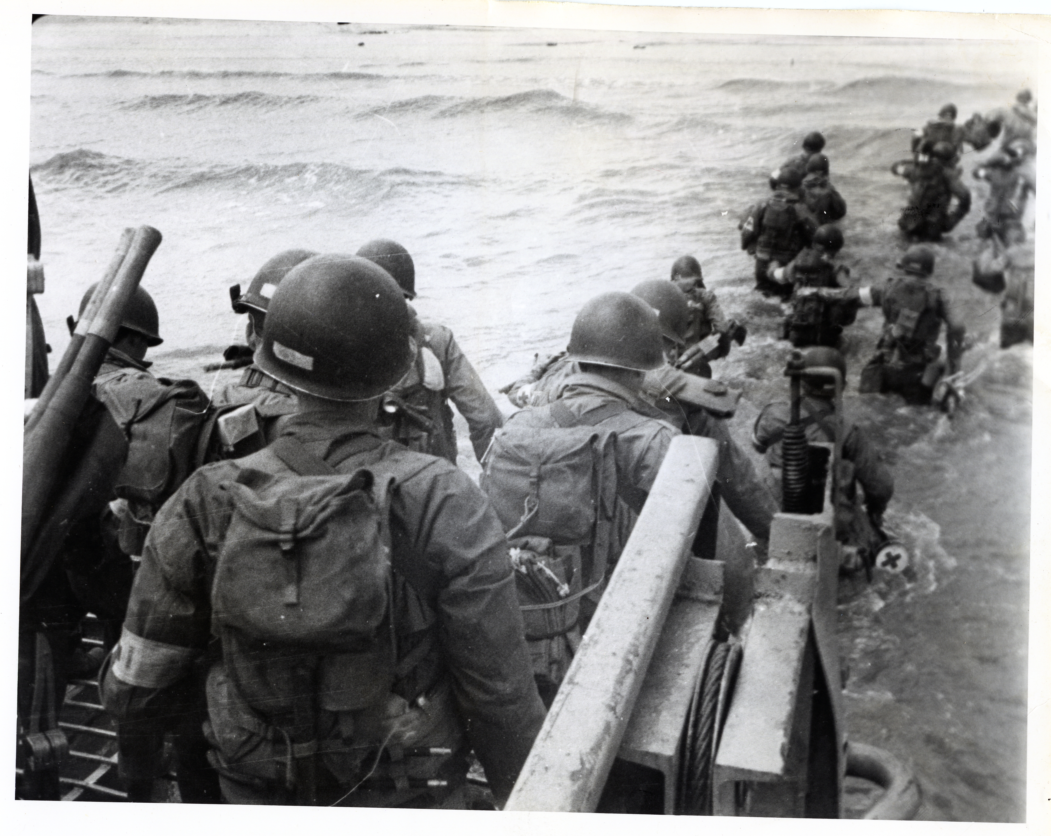 American soldiers with full equipment leaping from a landing craft into the surf and wading toward Utah Beach, 6 June 1944.